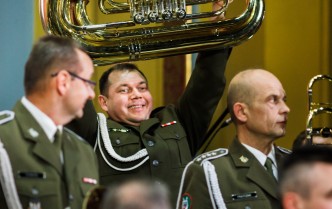 mężczyzna unoszący nad głowami muzyków wojskowych tubę