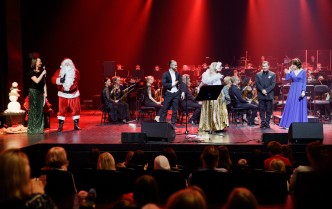 wokalistka, mężczyzna w stroju świętego Mikołaja i para taneczna wspólnie na scenie z dyrygentem i orkiestrą