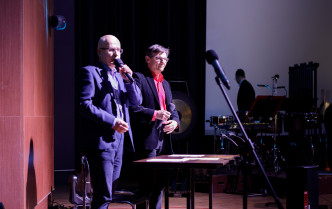 dwóch stojących mężczyzn, jeden z nich mówi do mikrofonu