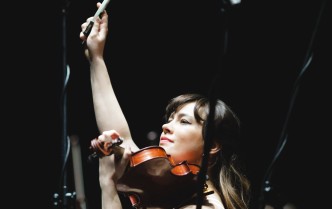 kobieta grająca na skrzypcach z uniesioną ręką, w której trzyma smyczek