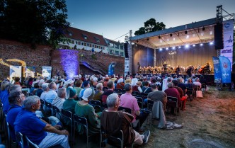 Widownia siedząca na krzesłach, która ogląda koncert na scenie