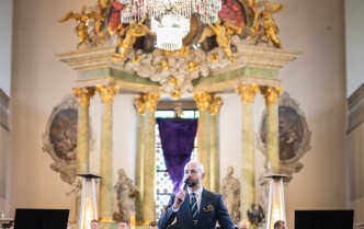 meżczyzna w granatowym garniturze mówi do mikrofonu, w lewej rce trzyma teczkę