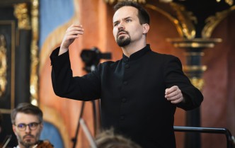 męczyzna w czarnym garniturze stoi z uniesionymi w górę rękoma - dyrygent