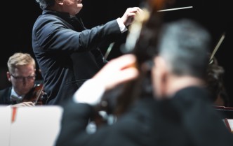 mężczyzna z uniesioną ręka, w której trzyma batutę