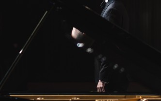 mężczyzna w czarnym garniturze stoi przy fortepianie