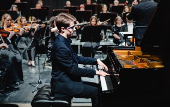 młody mężczyzna w ciemnym garniturze gra na fortepianiu