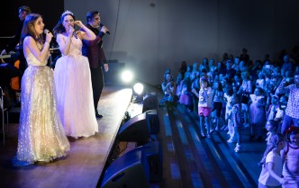 dwie kobiety i mężczyzna śpiewają do mikrofonów