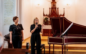 dwie kobiety stoją obok klawesynu, jedna z nich mówi do mikrofonu