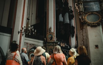 grupa turystów ukazana w dolnej części fotografii, głównie same głowy ludzi, patrzący na organy kościelne nad nimi