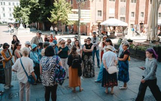 grupa turystów idąca przez rynek staromiejski w Toruniu, ludzie ukazani od tyłu