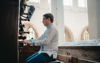 mężczyzna siedzący za organami grając na nich, ukazany z boku
