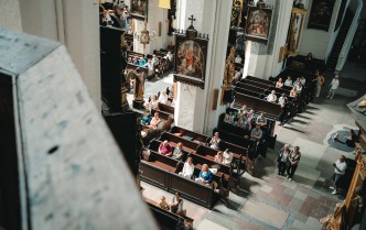 zdjęcie wykonane z góry, ukazuje publiczność siedzącą w kościelnych ławkach
