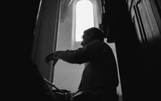 czarno-białe zdjęcie, mężczyzna ukazany z dolnej perspektywy od pasa w górę, grający na organach