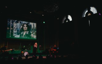 kobieta śpiewająca do mikrofonu, mężczyźni grający na gitarze, zestawie perkusyjnym i instrumentach klawiszowych