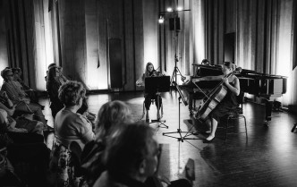 dwie kobiety grające na skrzypcach i wiolonczeli, i mężczyzna grający na fortepianie