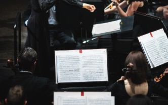 dyrygentka z uniesionymi rękomawśród grupy osób grających na instrumentach smyczkowych