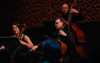 kobieta i męzczyzna grający na wiolonczelach, za nimi męczyzna grający na kontrabasie