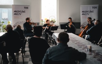 czworo muzyków grających na instrumentach smyczkowych, przed którymi siedzi publiczność