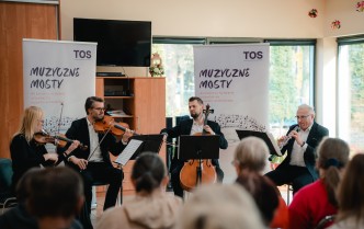 czworo muzyków grających na instrumentach muzycznych, przed którymi siedzi publiczność