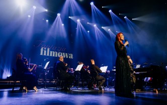 kobieta śpiewająca do mikrofonu, w tle siedzi orkiestra