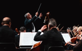 dyrygent z podniesionymi rękoma, w prawej dłoni trzyma batutę