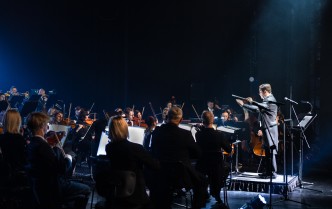 orkiestra i dyrygent na scenie widziani z boku orkiestry