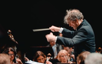 mężczyzna trzymający ręce w górze, w prawej dłoni trzyma batutę