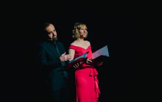 mężczyzna w czarnym garniturze i kobieta w czerwonej sukni mówiący do mikrofonów