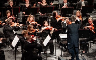 muzycy grający na instrumentach smyczkowych - skrzypce i altówki, przed nimi stoi dyrygent