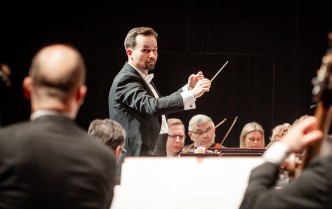 mężczyzna z uniesionymi rękoma, w lewej dłoni trzyma batutę