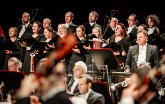 mężczyźni grajacy na instrumentach dętych i kotłach, za nimi chórzyści