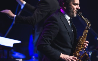 mężczyzna grający na saksofonie tenorowym, za nim stoi dyrygent