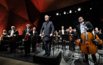 stojący na scenie dyrygent i orkiestra