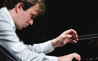 zbliżenie na pianistę w białej koszuli, pochylony nad klawiaturą z podniesioną jedną dłonią, mężczyzna ukazany jest z profilu