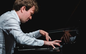 zbliżenie na pianistę w białej koszuli, pochylony nad klawiaturą z obiema dłońmi na klawiszach, mężczyzna ukazany jest z profilu