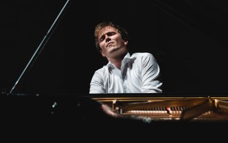 pianista ukazany od przodu, od klatki piersiowej w górę między klapą fortepianu a jego pudłem rezonansowym