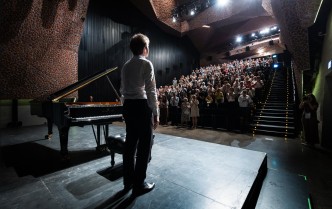 pianista ukazany na stojąco przy fortepianie od tyłu, przed nim rozświetlona pełna widownia