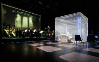 widok na scenę z dużym sześcianem, za króym siedzi orkiestra