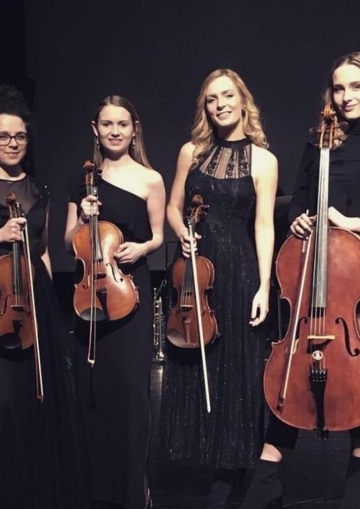 four young women in dark dresses standing and holding string instruments
