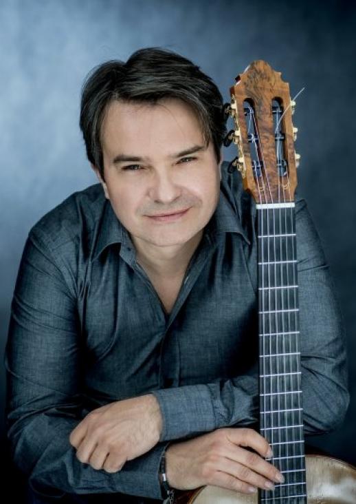 portrait of a man in a gray shirt, leaning against the neck of a guitar