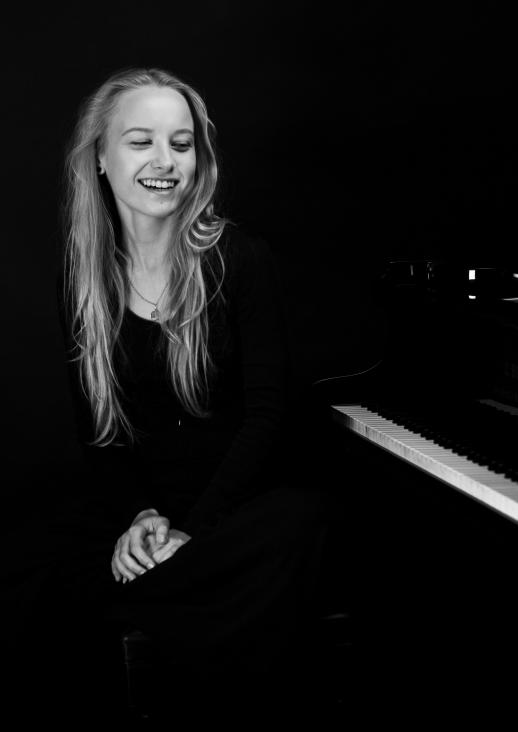 uśmiechnięta młoda kobieta siedząca przy fortepianie