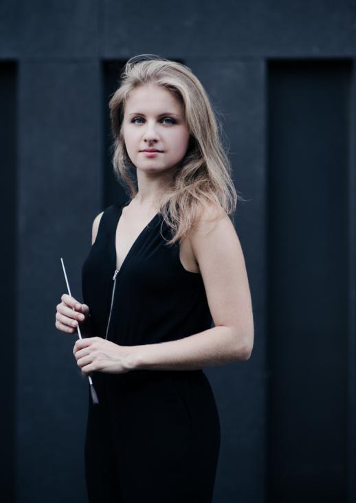 a young blonde woman in a black blouse holding a baton in her hands