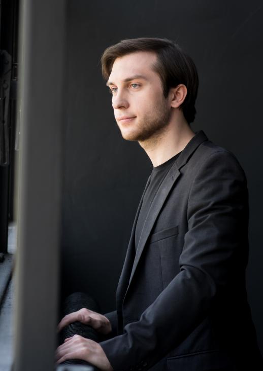 A young man with dark hair in a black shirt, looking out the window