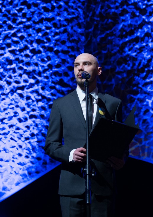 mężczyzna w zielonej koszulce i okularach mówiący do mikrofonu