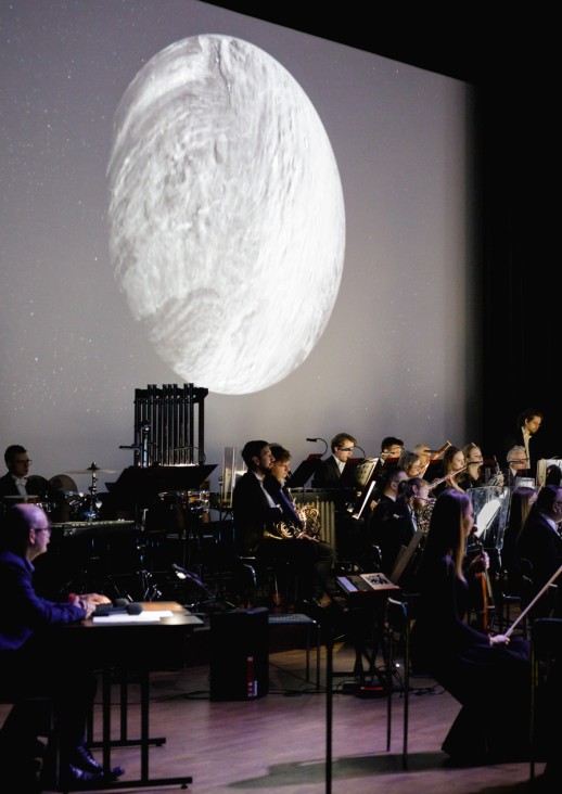 orkiestra na scenie, na tle wyświetlanej planety