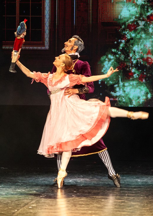 dziewczynka z uniesioną nogą trzyma lalkę w ręce, za nią stoi starszy mężczyzna - para baletowa