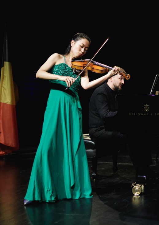 kobieta grająca na skrzypcach, za nią siedzi mężczyzna grający na fortepianie