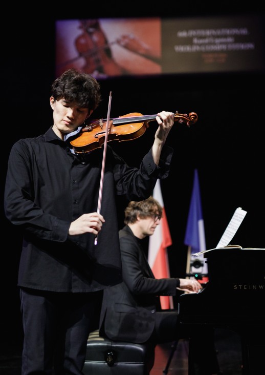 młody mężczyzna gra na skrzypcah, za nim mężczyzna grający na fortepianie