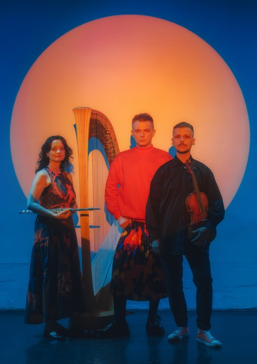 kobieta i dwóch mężczyzna stojących na niebieskim tle z pomarańczowym kołem