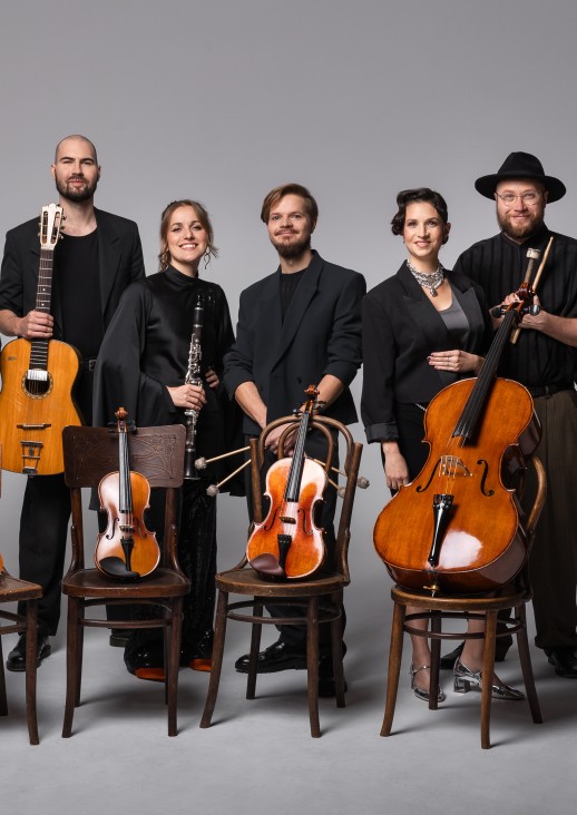 zdjęcie 7 muzyków warszawskiej orkiestry sentymentalnej, ubrani na czarno, stojący na wprost kamery, ukazani w całości, przed sobą mają instrumenty strunowe